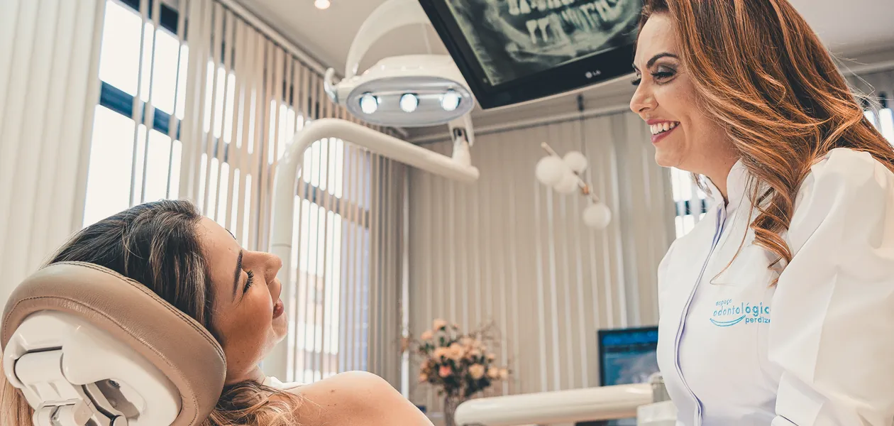 Dentista do Espaço Odontológico conversa com uma paciente sorridente na cadeira do consultório